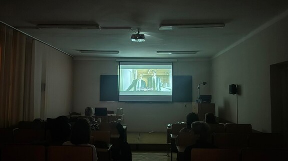 Przyciemniona sala wypełniona uczestnikami, w której wyświetlono film z rzutnika
